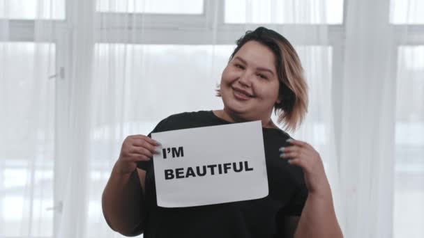 Käsite kehon positiivisuus - lihava nainen pitää merkki kaiverrus IM BEAUTIFUL - katsot kameraan — kuvapankkivideo