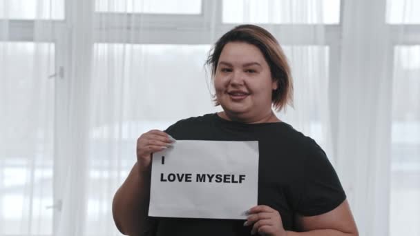 Concepto de positividad corporal - una mujer gorda sonriente sostiene un signo con la inscripción I LOVE MYSELF - mirando a la cámara — Vídeo de stock