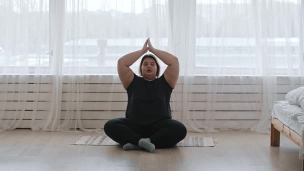 Una mujer gorda sentada en la posición de loto y haciendo yoga en casa — Vídeo de stock