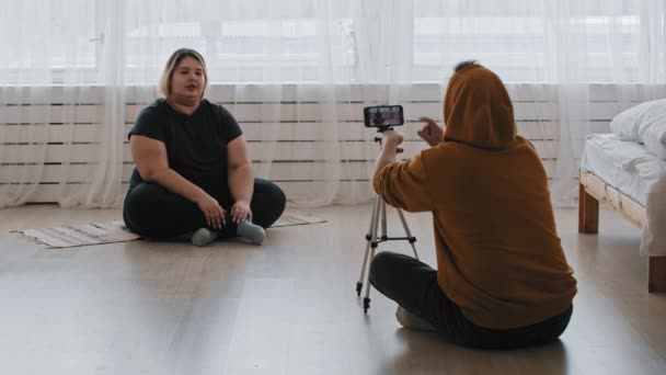 Cute confident overweight woman feminist and her friend sitting on the floor and recording a video for her followers — Stock Video