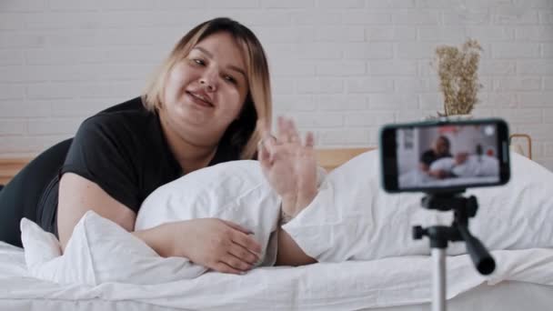 Una mujer con sobrepeso y confianza feminista acostada en la cama y haciendo un video para sus seguidores sobre la positividad corporal — Vídeos de Stock