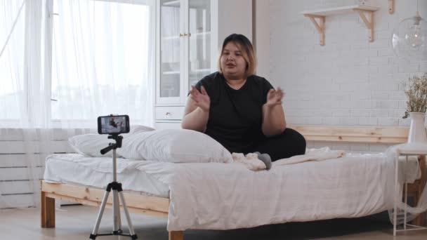 自信に満ちた太りすぎの女性フェミニストがベッドに座り、フェミニズムと身体のポジティビティについてのビデオで話しています。 — ストック動画