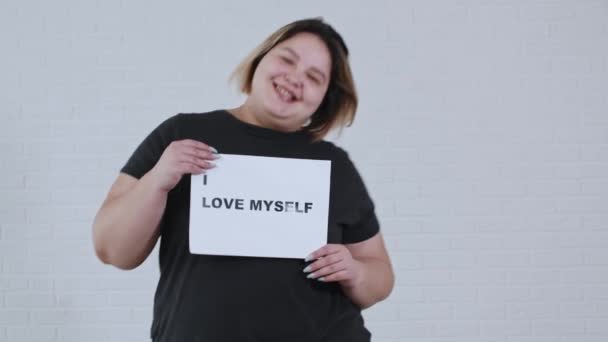 Концепция тела позитивности - пухленькая улыбающаяся женщина танцует и держит знак с надписью Я люблю себя — стоковое видео