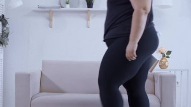 Şişman bir kadın kanepeye oturur ve evde kitap okur.