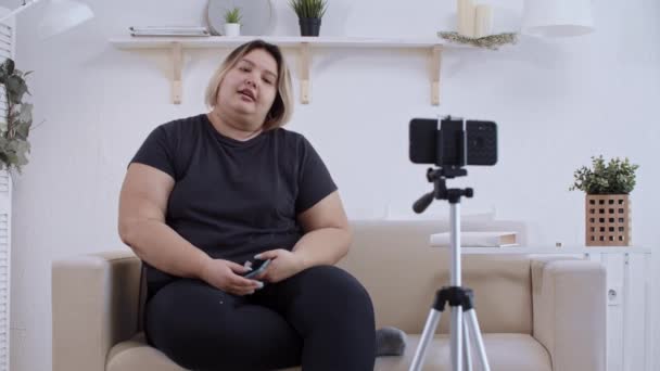 Body positiviteit - zelfverzekerde dikke vrouw feminist liggend op een bank en het maken van een video op haar telefoon voor haar volgelingen over positiviteit van het lichaam — Stockvideo