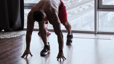 Stüdyoda panoramik pencereli kassız bir adam ısınıyor.