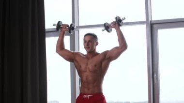 Spor eğitimi - atletik tişörtsüz adam halterlerle el kaslarını çalıştırıyor.