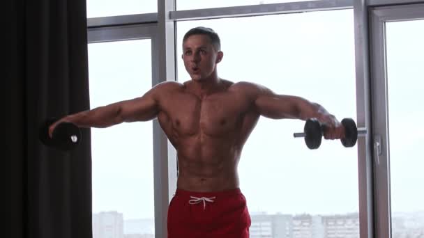 Atletický svalnatý muž bez trička trénuje ruce s činkami — Stock video