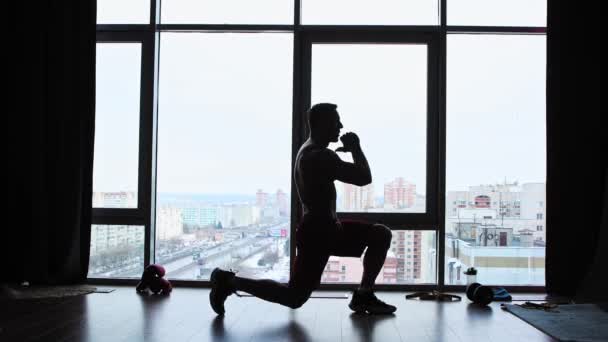 Sportoktatás a panoráma ablakos stúdióban - egy félmeztelen, izmos férfi sziluettje, aki bemelegíti a testét — Stock videók