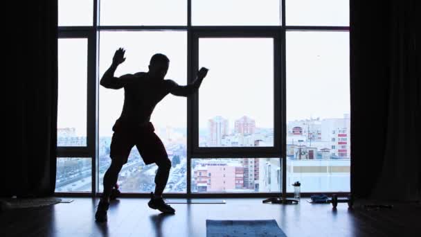 在有全景窗户的演播室里进行的体育训练- -一个赤身裸体、肌肉发达的男子跳下地板的轮廓- -耐力训练 — 图库视频影像