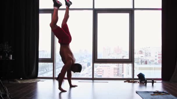 Entrenamiento deportivo en estudio con ventanas panorámicas - hombre musculoso sin camisa caminando sobre sus manos — Vídeo de stock