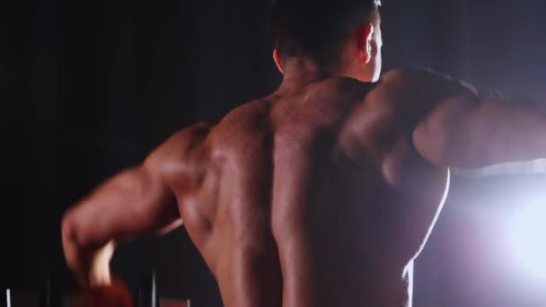 Entrenamiento deportivo - hombre atlético musculoso sin camisa que entrena sus manos en iluminación de contraste - vista desde la espalda — Vídeos de Stock