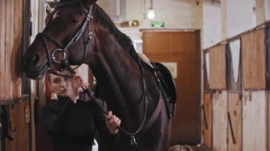 Bir kadın koşum takımı takıyor ve atı gezintiye hazırlıyor.