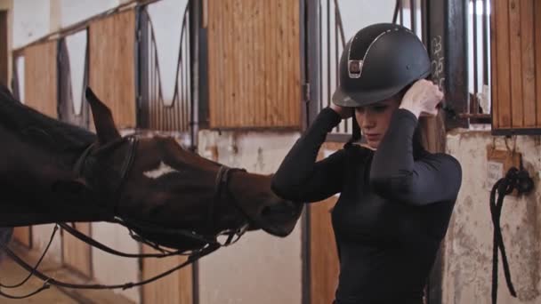 Eine Reiterin setzt einen Plastikhelm auf, der in der Nähe des Pferdes steht — Stockvideo