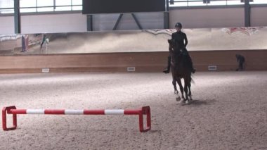 Binici- siyah elbiseli bir kadın hipodromda siyah bir ata biner ve engelin üzerinden atlar.