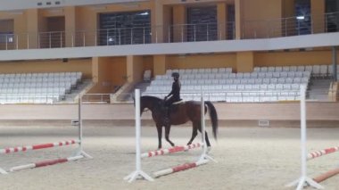 Equestrian - a woman in black clothes slowly rides a brown horse on an empty arena