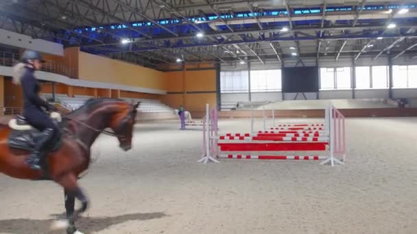 घोडेस्वार क्रीडा काळ्या कपड्यांमधील एक स्त्री अडथळ्यांभोवती घोड्यावर धावते — स्टॉक व्हिडिओ