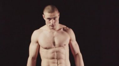 Siyah bir stüdyoda genç bir sporcu elleri başının arkasında kameraya bakar.