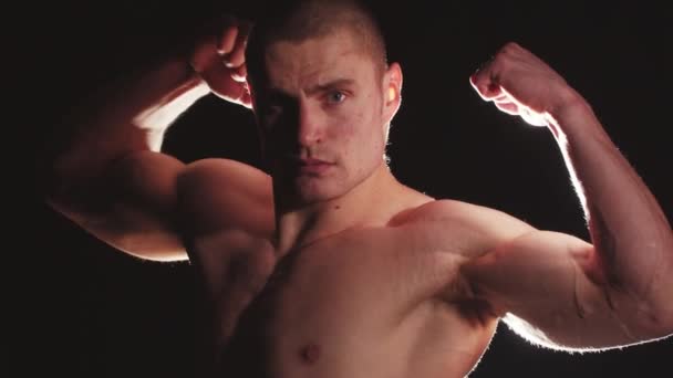 Joven chico guapo mostrando sus músculos en contraste brillante iluminación detrás de él — Vídeos de Stock