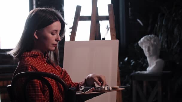 Uma jovem mulher em oficina de arte pega um pincel e está prestes a desenhar uma pintura — Vídeo de Stock