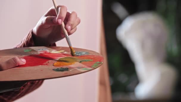 Молода жінка в художній майстерні наносить помаранчеві та сині кольори на палітру — стокове відео