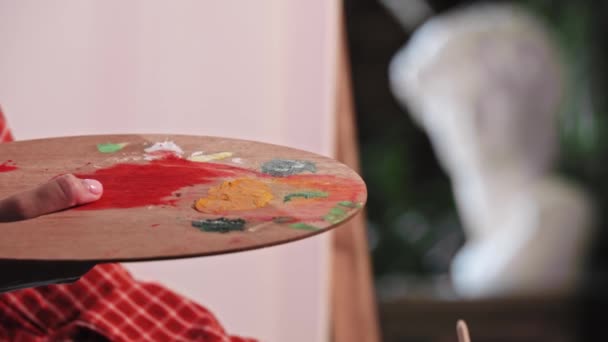 Une jeune femme dans un atelier d'art mettant une couleur orange et bleue sur la palette et la mélangeant — Video