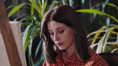 Stüdyoda yeşil bitkilerle oturan genç ve güzel bir kadın sanatçı.