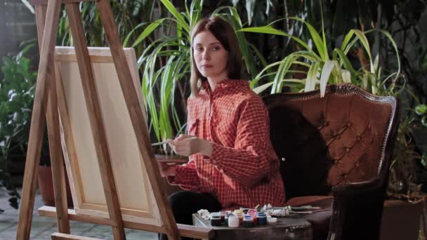 Artista en un taller - joven mujer bonita dibujando una pintura - mirando a la cámara — Vídeos de Stock