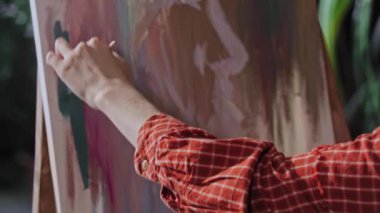 Genç bir kadın stüdyodaki bir tuvale soyut bir resim çiziyor.