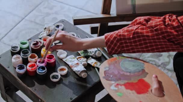 Mujer joven dibujando una pintura - mezclando colores en una paleta de madera — Vídeo de stock