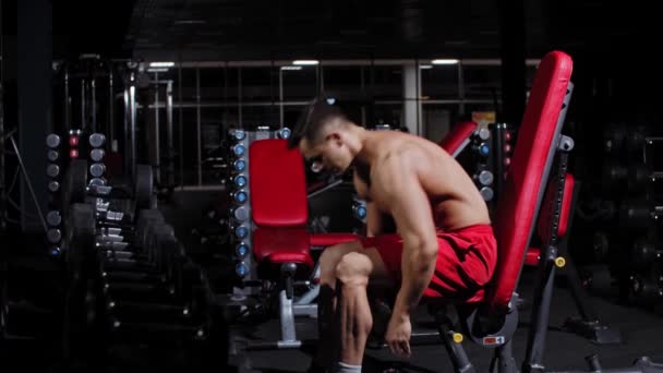Gepompte man zit op een fitnesstoestel en begint met het heffen van halters — Stockvideo
