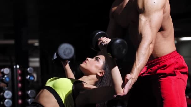 Женщина качает мышцы рук с тренером, помогающим ей — стоковое видео