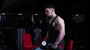 Spor salonu eğitimi. Genç, formda bir adam dambıl kaldırıyor.