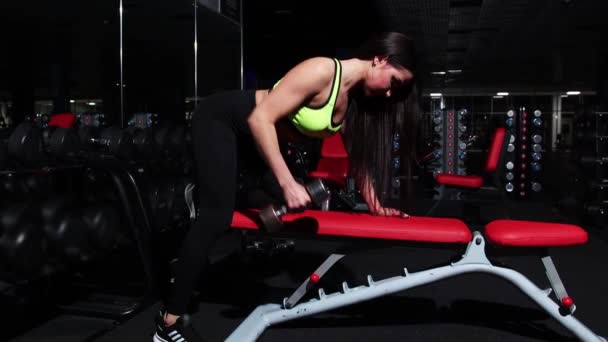 Entrenamiento en el gimnasio - mujer bombeando los músculos de sus manos - apoyando su rodilla en el soporte y levantando la mancuerna — Vídeos de Stock