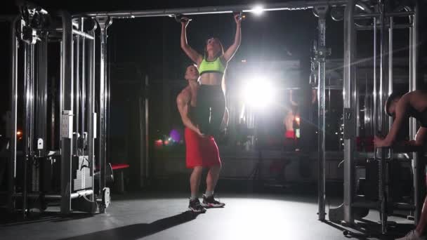 Treinamento de ginástica - grupo de amigos treinando - uma mulher aprendendo a puxar para cima com a ajuda de seu amigo e outro homem filmando-os no telefone — Vídeo de Stock