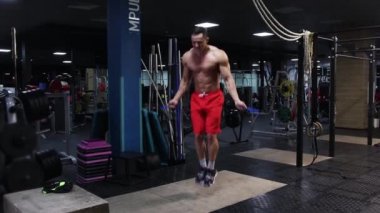 Boş bir spor salonunda antrenman. Formda bir adam halatın üzerinden atlıyor.