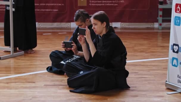 RUSSIA, KAZAN 24-04-2021: Kendo turnuvası - erkek ve kadın yerde oturuyor ve kavgaları telefonlarıyla kaydediyor — Stok video