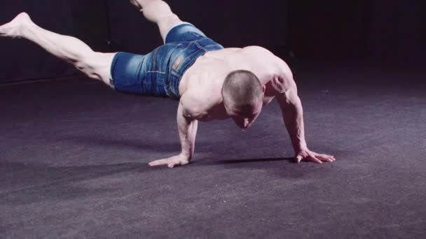 Молодий хлопець в джинсових шортах балансує своє тіло стоячи на одній руці — стокове відео
