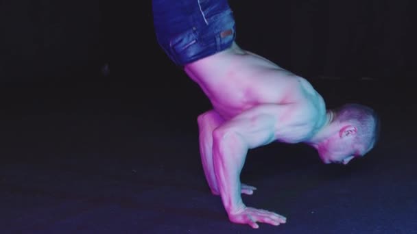 Молодий хлопець в джинсових шортах, що стоять на руках в студії з неоновим освітленням — стокове відео