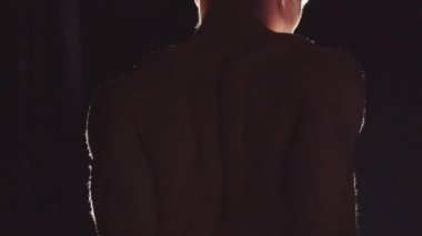 Arkasından parlak kontrastlı aydınlatma ile vücudunu esneten genç, güzel görünümlü bir adam.