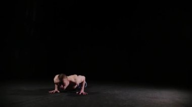 Genç bir sporcu ters takla atıyor ve siyahi stüdyoda şınav çekiyor.