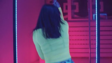 Kulüpte neon ışıklı direğin yanında dans eden yetişkin bir kadın.