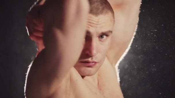Jong goed uitziende pumped-up guy tonen zijn spieren in fel contrast verlichting achter hem — Stockvideo