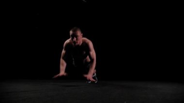 Genç yarı çıplak pompalı adam karanlık arenada şınav çekiyor.