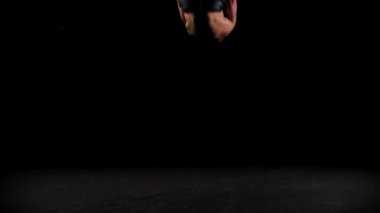 Genç pompalı adam karanlık arenada taklalar atıyor.