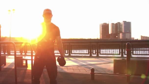 Fiatal sportos férfi gyakorolja a kezét súlyzókkal naplementekor. — Stock videók