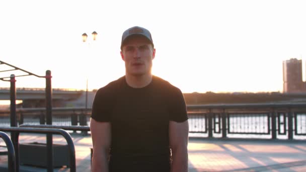 Joven deportista entrenando sus manos con pesas al aire libre al atardecer mirando a la cámara — Vídeos de Stock