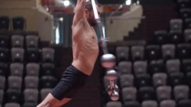 Sirk arenasında akrobatik bir adam performans inşaatında ayağa kalkıyor ve yükseliyor.