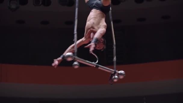 Acrobatic man training at the circus arena - hanging upside down on the rotating performance construction holding on it with his mouth — Stock Video