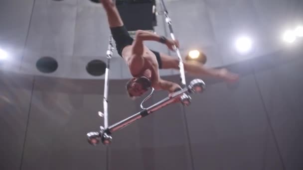 Acrobatic man på cirkus arenan - hängande upp och ner på roterande prestanda konstruktion hålla på den med munnen — Stockvideo